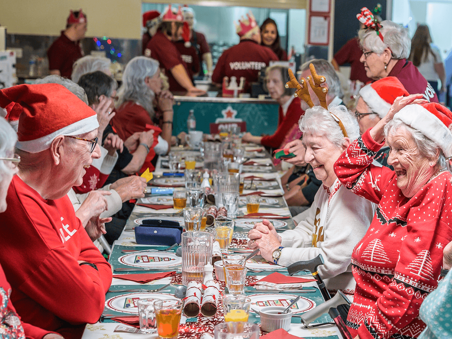 A group of older people enjoying a Festive Spread Christmas meal at a community centre being served volunteers