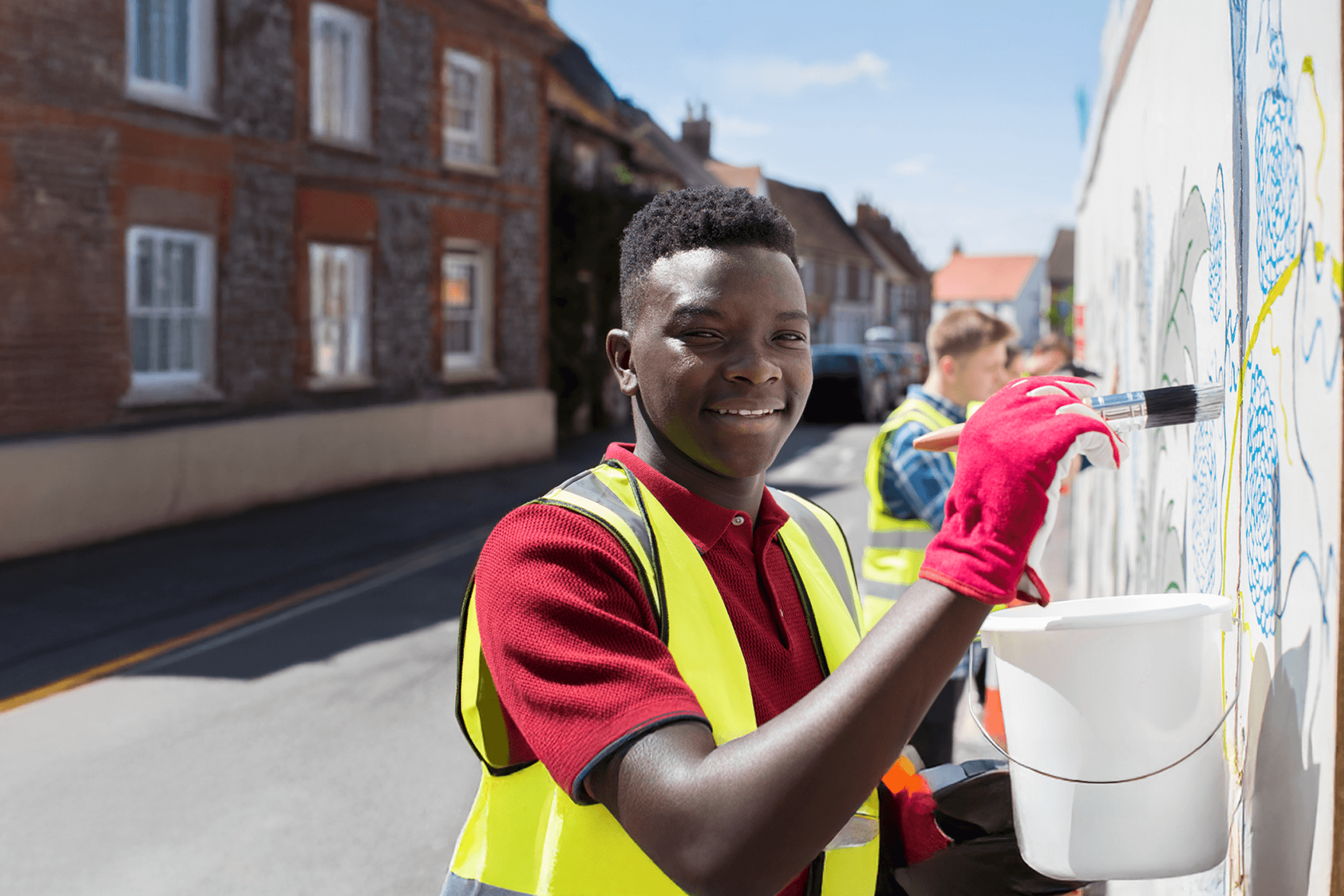 A young man outside painting a wall on a street wearing a reflective vest