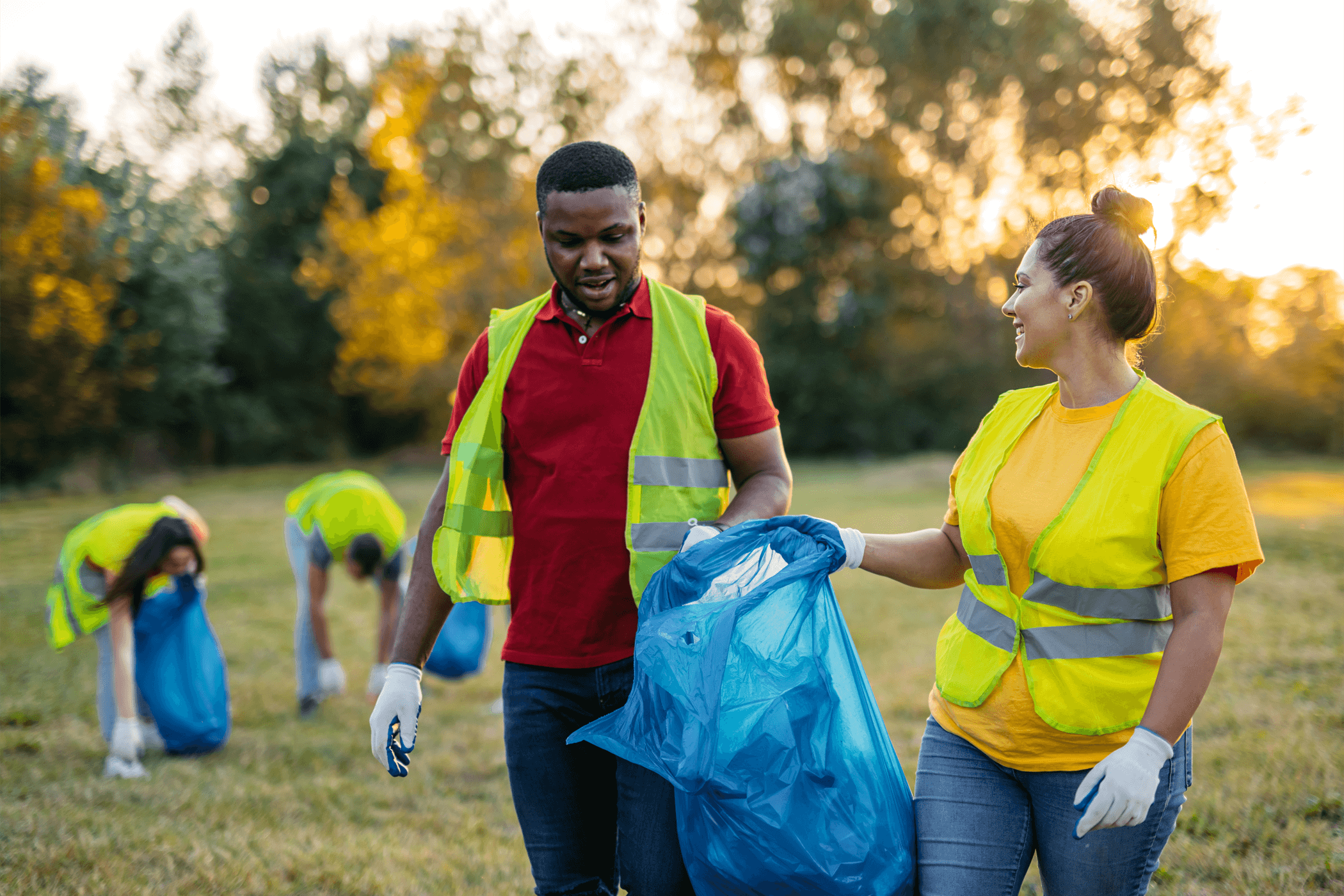 Two young people collecting litter outdoors both wearing gloves and reflective vests