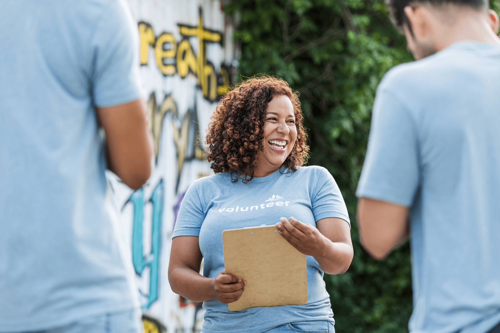 A female volunteer wearing a light blue T-shirt, smiling and looking happy with a clipboard