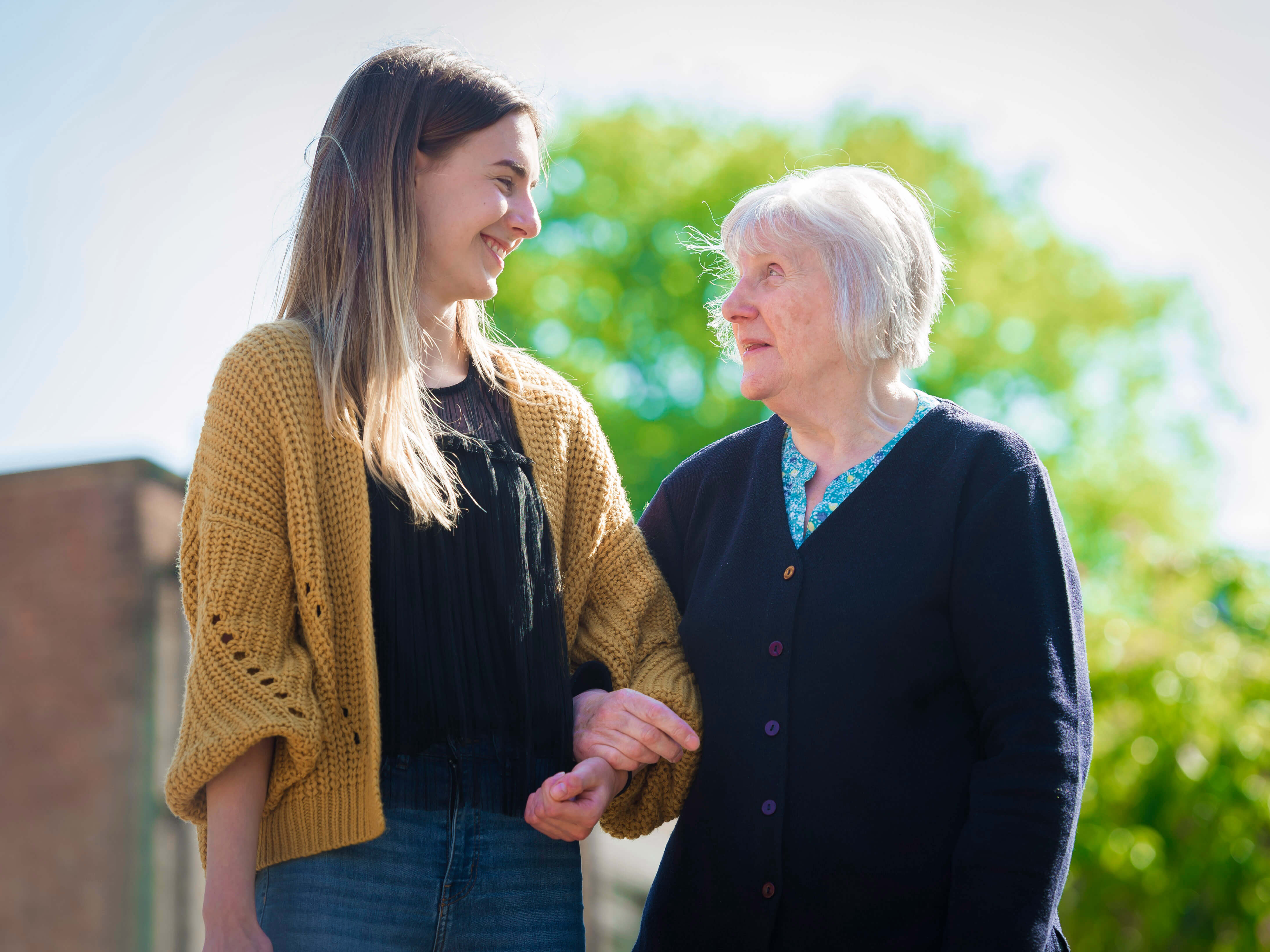 A young volunteer linking arms with an older woman and smiling 